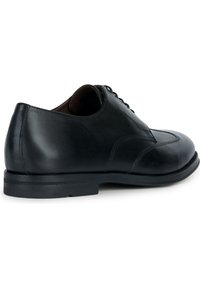 Chaussure habillée en cuir noir avec une texture lisse, bout arrondi, couture contrastante et une semelle en caoutchouc noir basse. Lacets visibles sur le dessus.
