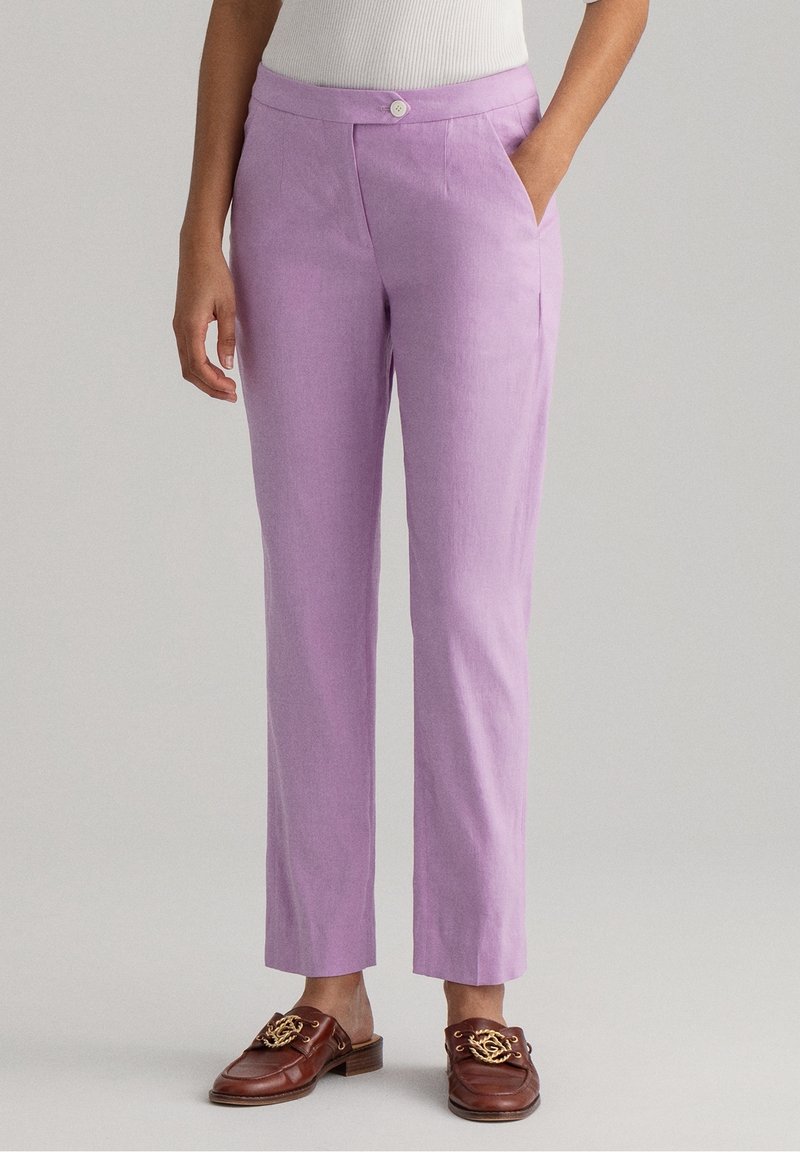 Světle fialové lněné kalhoty se rovný zástřihem, s předními kapsami a zapínáním na knoflík. Nosí se s hnědými mokasínami.