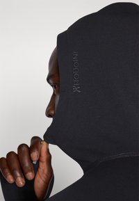 Black hooded sweatshirt featuring a smooth texture, fitted design, and integral thumbholes. Logo is embossed on the side of the hood.