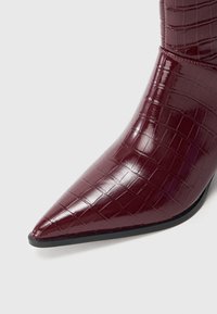 Burgundy ankle boot with a glossy, crocodile-embossed pattern, pointed toe, and stiletto heel. Solid black sole with minimal accents.