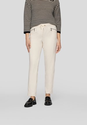 Cream-colored pants with a tapered fit, featuring front zip pockets and a drawstring waist, paired with a black and cream striped sweater.