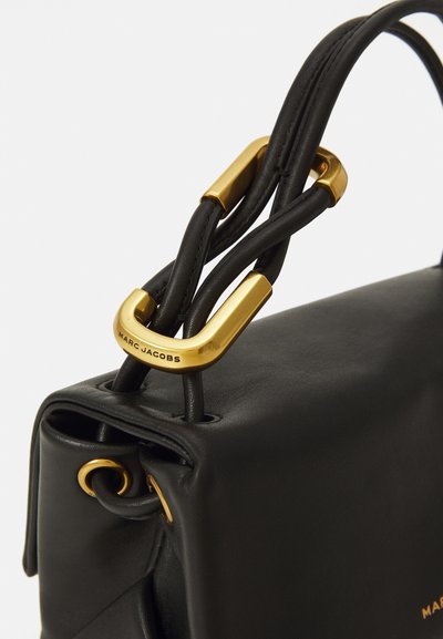 Bolso de mano de cuero negro con forma estructurada. Presenta herrajes dorados y un detalle de asa trenzada. Logotipo en el herraje. Textura suave.
