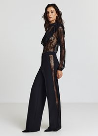 Top in pizzo nero con scollo arricciato abbinato a pantaloni neri a gamba larga e vita alta, con pannelli laterali in pizzo. Tessuto dalla texture liscia.