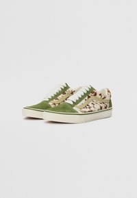 Las zapatillas de gamuza verde presentan un lateral con un estampado difuso en crema y marrón, cordones blancos y una suela de goma beige. Diseño casual de corte bajo.