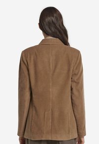 Brun manchesterblazer med en klassisk notch-krage, långa ärmar och ett texturerat ribbat mönster; skräddarsydd passform med en springa bak.