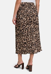 Gerimpelde zwart en tan luipaardprint rok met een elastische tailleband, die tot halverwege de kuit reikt, gecombineerd met zwarte hoogte sandalen.