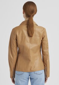 Helle Lederjacke mit tailliertem Design, ausgestattet mit einem Reverskragen und Reißverschlussmanschetten. Glatte Textur und Nahtdetails auf dem Rücken.