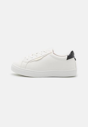 Białe niskie sneakersy z białymi sznurowadłami i podeszwą, z czarną zakładką na pięcie i gładką skórzaną cholewką, widoczne z boku.