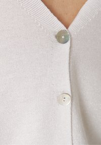 Ljusgrå stickad cardigan med V-ringning, som har två runda silverknappar och en subtil glans i tygtexturen.