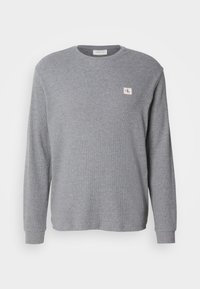 Γκρι μακρυμάνικος φούτερ από υφασμάτινη υφή, με στρογγυλή λαιμόκοψη και μικρό ρέλι CK στην επάνω αριστερή πλευρά.