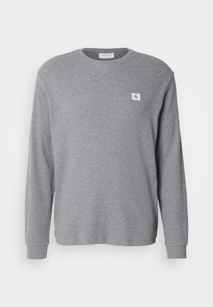 Sivi dukserica dugih rukava od teksturirane tkanine, s okruglim izrezom i malom CK logom na gornjoj lijevoj strani.