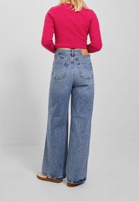 Höga blå vida jeans med en blekt textur och bakfickor, kombinerat med en långärmad rosa topp.