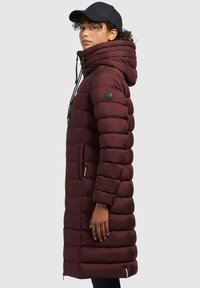 Manteau rembourré bourgogne avec un col montant, une capuche à cordon de serrage et des poches zippées. Caractéristiques d'un design matelassé horizontal et d'un patch logo sur la manche.