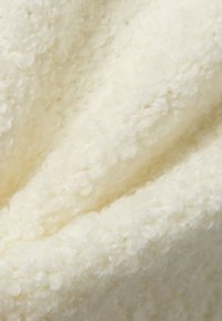 Tessuto crema strutturato con una superficie ad anello, caratterizzato da fibre morbide che creano profondità e calore in un disposizione liscia e drappeggiata.