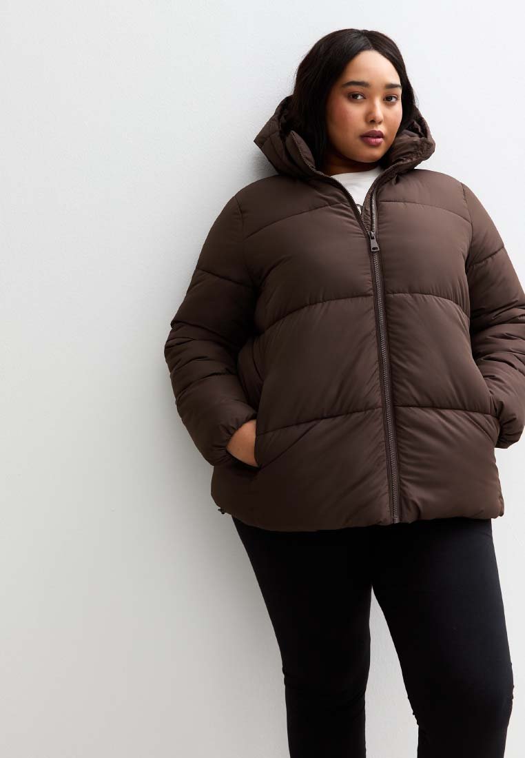 Brązowa ocieplana kurtka z kapturem, z zamkiem błyskawicznym z przodu i bocznymi kieszeniami. Tkanina wydaje się gładka, z miękką teksturą i pikowanym wzorem.
