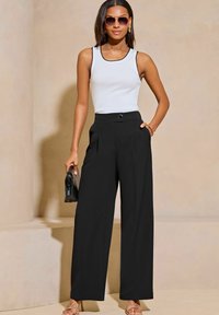 Pantaloni neri a vita alta plissettati con tasche laterali, abbinati a una canotta bianca con rifiniture nere, e accessoriati con occhiali da sole e una pochette.