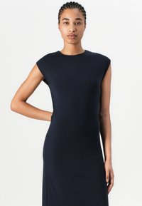 Ναυτικό μπλε, άνευ μανικιών φόρεμα με στενή γραμμή, στρογγυλή λαιμόκοψη και ασύμμετρη ραφή. Φτιαγμένο από λείο, ελαστικό ύφασμα.