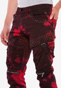 Rote und schwarze Batik-Denimhose mit Nietendetails, Cargo-Taschen, strukturiertem Rippstrick und mit Reißverschluss versehenem Unterschenkel.