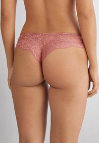 Kant boyshorts in een stofroze kleur met een bloemenpatroon, doorschijnende panelen en een golvende rand, die een delicate design benadrukken.