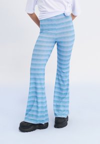 Leggings bleu évasés avec un motif ondulé dans des teintes plus claires, fabriqués dans un tissu lisse et extensible, assortis à des chaussures noires épaisses.