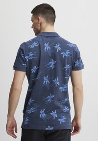 Marineblå kortermet polo skjorte med blå blomsterdesign, en klassisk krage og rett kant. Laget av mykt, teksturert stoff.