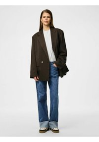 Pruun ribaülik, millel on laiad kraed, on kombineeritud valge T-särgiga ja kõrge vöökohtadega siniste teksadega, millel on narmendavad ääred. Pruunid tossud valgete aktsentidega.