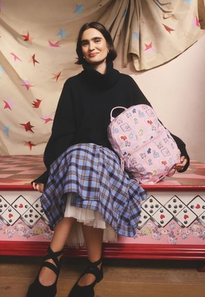 Roza nahrbtnik z igrivimi vzorci, črn ohlapen pulover, modra karo krilo in črni čevlji z diagonaliai trakovi.
