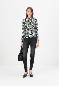 Haut à manches longues rayé noir et blanc porté avec un jean skinny noir et des ballerines à bout pointu. Accessoire : petit sac à main noir.