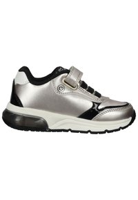 Zapatilla deportiva plateada con acentos en negro, parte superior sintética, banda de velcro y suela texturizada. Presenta una unidad de amortiguación de aire visible.