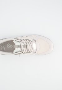 Lysebeige atletiksneaker med mesh-tå, snørebånd bundet og logo synlig inde i skoen, set fra oven på en hvid baggrund.