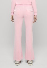 Rózsaszín, bővülő szárú melegítőnadrág puha anyagból, két gombos záródású hátsó zsebbel. Látható varrásokkal és szoros derékrésszel.