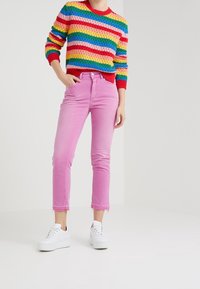 Jersey de punto con rayas del arcoíris y cuello rojo, combinado con jeans cortos rosa claro, de corte recto y dobladillo deshilachado, usados con zapatillas blancas.