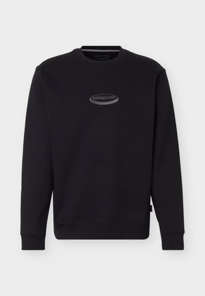 Crna majica dugih rukava s okruglim izrezom i malim sivim ovalnim logotipom Patagonia u sredini ispod prsa.