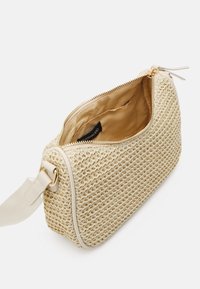 Woven straw taška v krémové barvě se hladkým béžovým zipem, hnědou látkovou podšívkou a texturovaným povrchem. Obsahuje ramenní popruh.