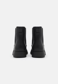 Czarne botki za kostkę wykonane z gładkiego materiału syntetycznego, charakteryzujące się minimalistycznym designem, płaską gumową podeszwą oraz dwoma pętlami do łatwego zakładania.