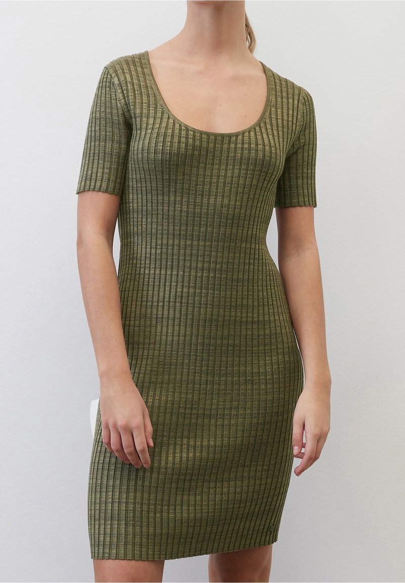 Femme portant une robe en maille côtelée ajustée, vert olive, à manches courtes et encolure dégagée, sur un fond uni.