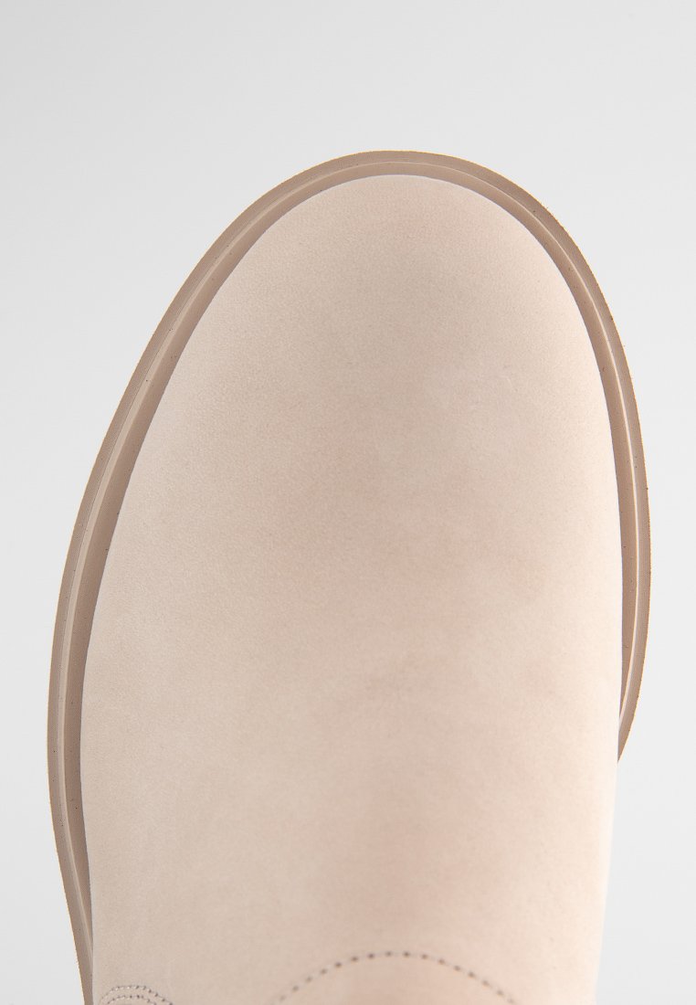 Hellbeige Knöchelstiefel aus weichem Wildleder mit abgerundeter Spitze, glatter Textur und dünner Gummisohle. Nähedetail entlang der Kante.