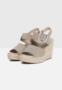Beige wedge sandals with open toe design, made of soft suede. Features a wide strap and adjustable buckle. Rope-wrapped platform sole.