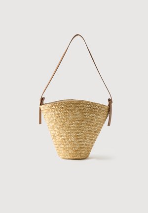 Bolso tipo cubo de paja tejido con base ancha, parte superior estrecha y correa de hombro ajustable de cuero marrón.