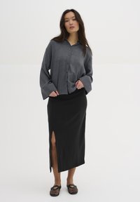 Grijze overhemd met brede mouwen, gecombineerd met een zwarte midi-rok met een zijsplit. Zwarte instap schoenen maken de look compleet.