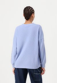 Lichtblauw, getextureerd lang mouw oversized shirt met een ronde halslijn, contrasterende accenten op de linkermouw en een relaxte pasvorm.