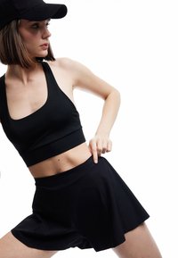 Top deportivo negro de corte corto con escote amplio, combinado con una falda corta negra. Las telas parecen suaves, ligeras y ajustadas, con un ligero brillo.