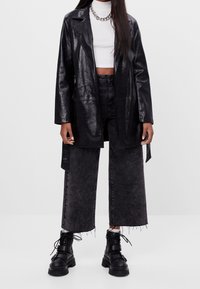 Czarna kurtka z sztucznej skóry o strukturowanym kroju i otwartym przodzie, w połączeniu z ciemnoniebieskimi, wysokopodwieszonymi kulotami i masywnymi czarnymi botkami.