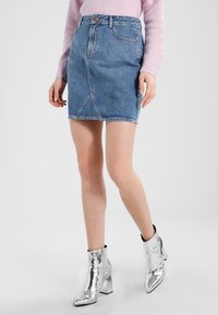 Denim A-linje kjol med ljusblåtvätt, detalj med framstygn och två framfickor. Kombinerad med glänsande silvriga klackstövlar.