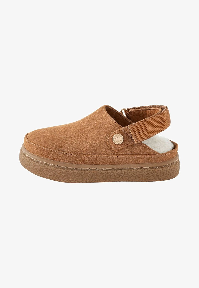 Brun mockaläder slip-on sko med en texturerad gummisula, justerbart bakrem och mjukt foder synligt vid hälen.