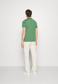 Polo shirt en coton vert avec un col, associé à un pantalon blanc. La chemise a des manches courtes et un design droit.