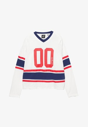 Cămașă albă cu mâneci lungi și decolteu în V, având dungi roșii și bleumarin și numărul „00” în roșu îndrăzneț. Material moale din bumbac.