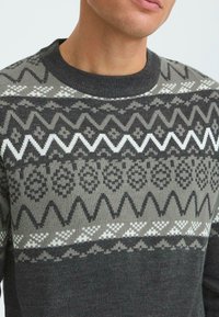 Dunkelgrauer Pullover mit Rundhalsausschnitt, der ein geometrisches Muster in Schwarz- und Weißtönen aufweist. Weiche Textur mit gestrickten Details.