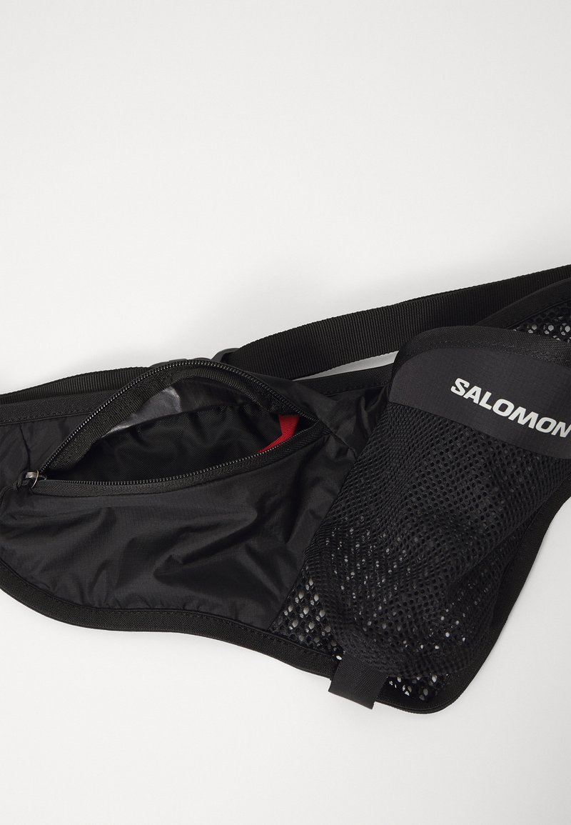 Black waist pack with a mesh pocket, zip closure, and adjustable strap. Features a red lining inside the main compartment for contrast.