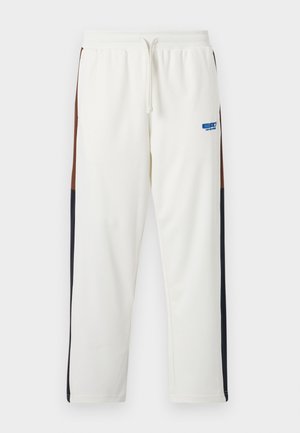 Hvite sweatpants med snøring i livet, med brune og marineblå sidelapper. Myk stoff med en blå logo på venstre lår.